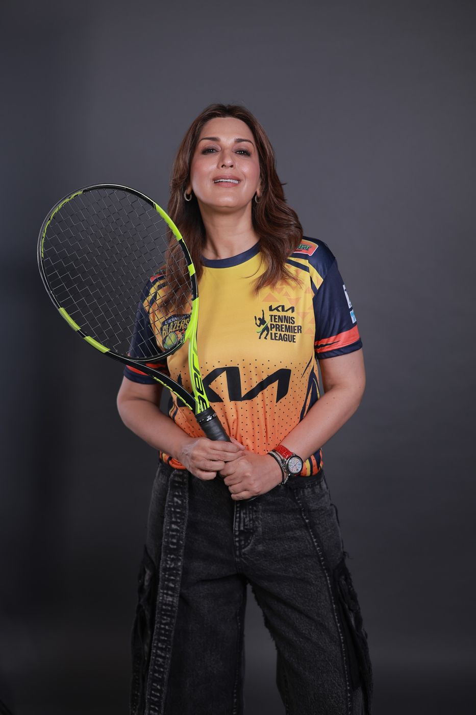 Sonali Bendre with a tennis racket in the Lucknow Blazers jersey